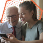 A young lady and an older gentleman looking at what seems like a smart phone.